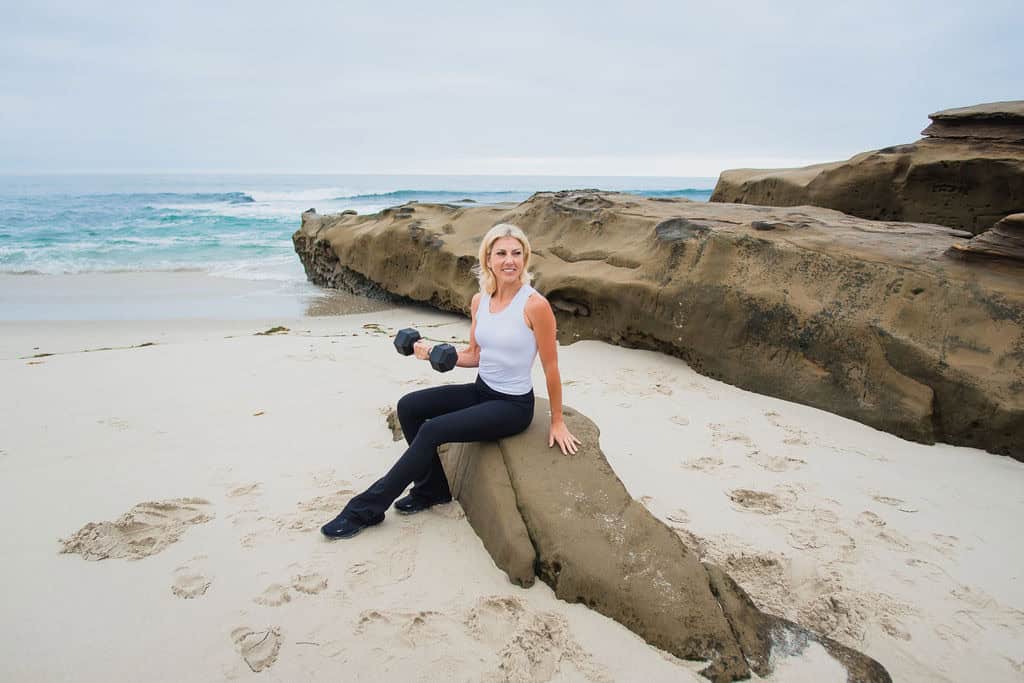 Rose Martin seated on a sandstone rock holding a dumbbell